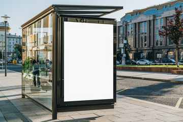 vertical blank white billboard at bus stop on city street. in the background buildings and road. moc