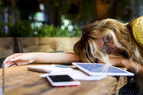 Fotografie, Obraz Young pretty woman tired of work lying on table in front of laptop and taking a