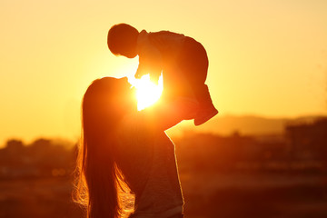 Mother raising her kid son at sunset with the sun in the middle