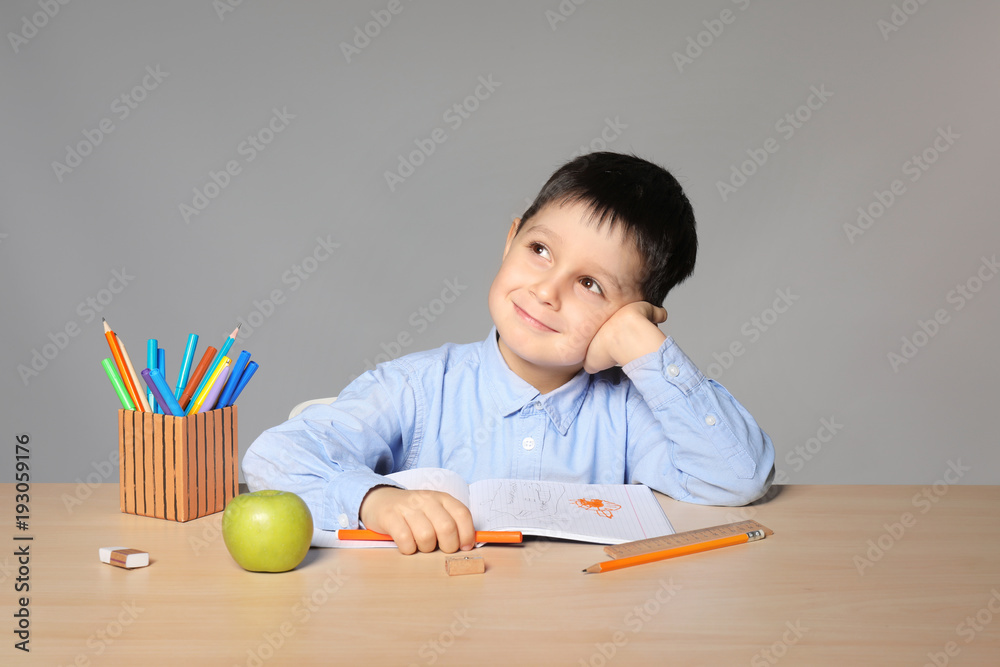 Cute little boy doing homework against grey background