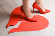 Woman stepping on broken paper heart on floor. Relationship problems