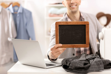 Wall Mural - Man holding mini chalkboard in atelier. Small business owner