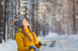 © kristinakibler - Portrait of young smiling woman looking to falling snow in a winter forest