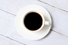 Top View Of Black Coffee Inside White Cup On White Wooden Background.