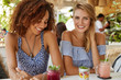 © WHstudio Leushin N - Pleased multiethnic lesbian couple spend spare time at cozy cafeteria, taste exotic smoothie, have cheerful expressions, recreat together in hot tropical country, glad to relax. Friendship concept