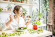 © rh2010 - Young woman eating healthy food sitting with smartphone in the beautiful interior with green flowers on the background