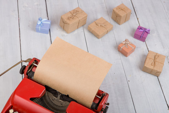 Holidays concept - red typewriter with blank craft paper, gift boxes on white wooden background