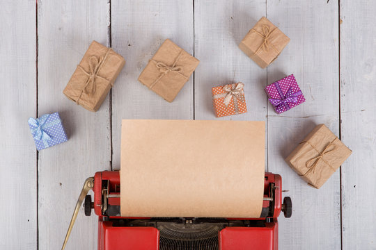 Holidays concept - red typewriter with blank craft paper, gift boxes on white wooden background