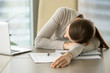 Tired female office worker lying on desk with laptop and business documents because of overwork. Exhausted from hard paperwork businesswoman sleeping on workplace, taking short napping during work day