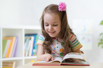 little smart child girl looking at book while sitting at table in nursery