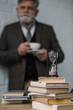 © LIGHTFIELD STUDIOS - blurred senior man drinking coffee with stack of books and hourglass on foreground