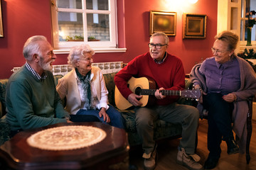 Wall Mural - Old senior man playing guitar with his friends, making great party