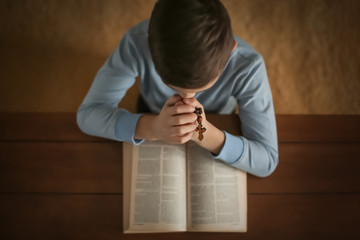 Wall Mural - Little boy with cross praying over Bible at table