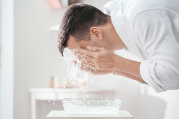 man spraying water on his face after shaving in bathroom