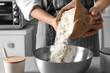 Woman pouring flour into bowl on table