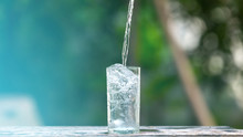 Drink Water Pouring In To Glass Over Sunlight And Natural Green Background.Select Focus Blurred Background.