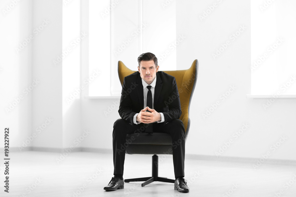 Handsome businessman sitting in comfortable armchair indoors
