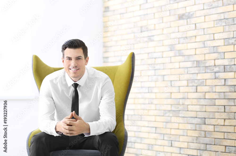Handsome businessman sitting in comfortable armchair indoors