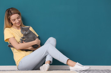 Wall Mural - Young woman with cute pet cat against color wall