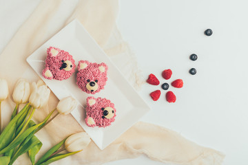 Wall Mural - top view of delicious muffins in shape of bears, fresh berries and tulip flowers