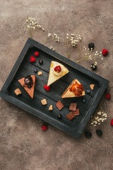 Wall Mural - top view of pieces of delicious cakes with chocolate and berries on wooden tray
