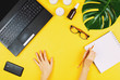 © lavrenkova - Business flatlay with laptop, mobile phone, glasses, philodendron leaf, candles, cream and woman's hands holding pen. Concept of a woman's work place. Flat lay. Yellow background.