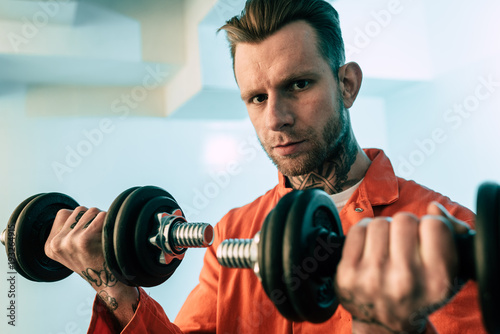 Tattooed Prisoner Training With Dumbbells In Prison Room