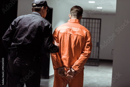 Fotografía rear view of prison officer leading prisoner in handcuffs in corridor