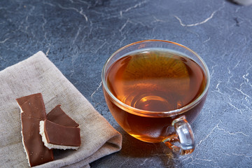 glass cup of black tea with chocolate pieces on a dark greyish marble background. Top view