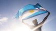 Young man holding argentinian national flag to the sky with two hands at the beach at sunset argentina