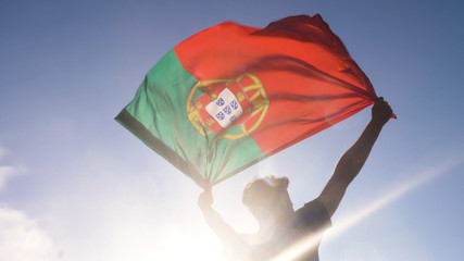 Wall Mural - Young man holding portuguese national flag to the sky with two hands at the beach at sunset portugal