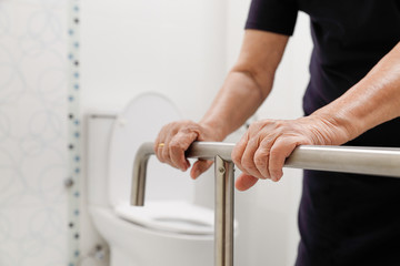 Elderly woman holding on handrail in bathroom.