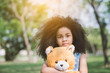 © saksit - Little cute african american girl hugging embraces an amusing teddy bear against summer nature.