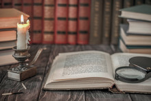 On The Wooden Background Of The Table There Are Stacks Of Colorful Books Near The Old Candlestick With Burnt Matches Lying Next To Each Other.