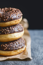 Stack Of Three Chocolate Donuts On A Kraft Paper Against Black Wall.