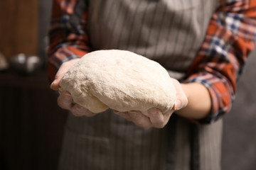 Wall Mural - Young woman holding raw dough in kitchen, closeup