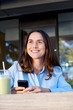 © mimagephotos - attractive older woman relaxing outside with a drink and cellphone in hand