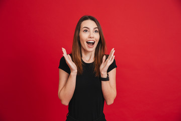 Poster - Portrait of young happy woman 20s raising arms and shouting in excitement, isolated over red background