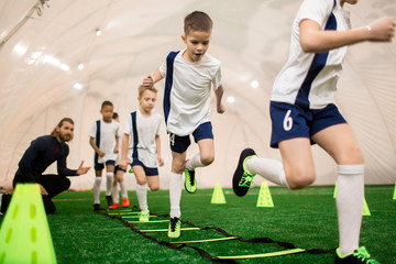 row of boys running on green football field during training with instructor