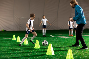 Young trainer and team of little boys playing or training on green lawn