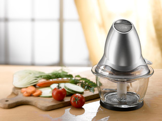 mini food processor and chopped vegetables on a wooden table. light comes from a window in the background