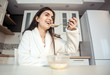 © proimagecontent - Beautiful girl wears white bathrobe eating cornflakes with milk in the kitchen in the morning