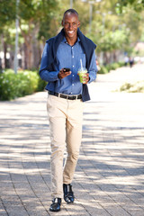 Wall Mural - Full length happy african american man walking with mobile phone outdoors