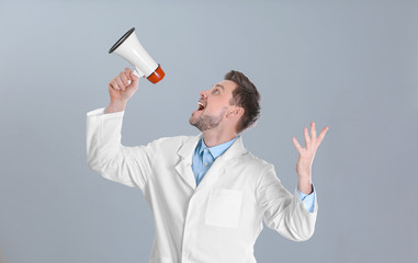 Wall Mural - Male doctor with megaphone on grey background