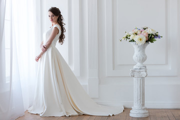 beautiful bride posing in elegant wedding dress near bouquet of flowers in vase