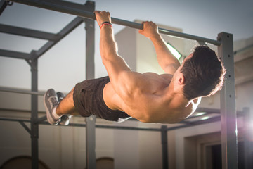 Handsome muscular man doing exercises on horizontal bar outdoors. Calisthenics workout.