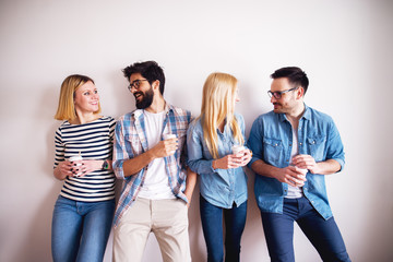 Group of young colleague people standing against the wall drinking coffee in paper cups and talking for a break.