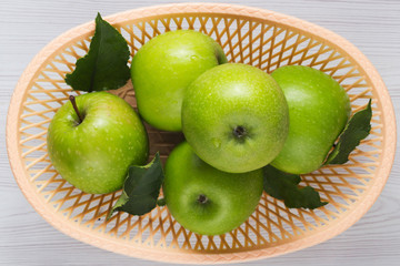 Wall Mural - Green apples with leaves in a basket on white wooden table Top view