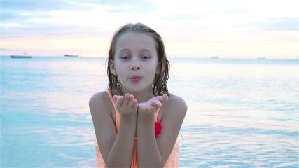 adorable little girl at beach having a lot of fun at sunset. happy kid looking at camera and kissing