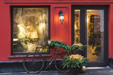 Christmas Decorated Showcase With Old Bicycle, Fir Branches, Glass Shiny Toys And Vintage Lantern. Red Building Facade